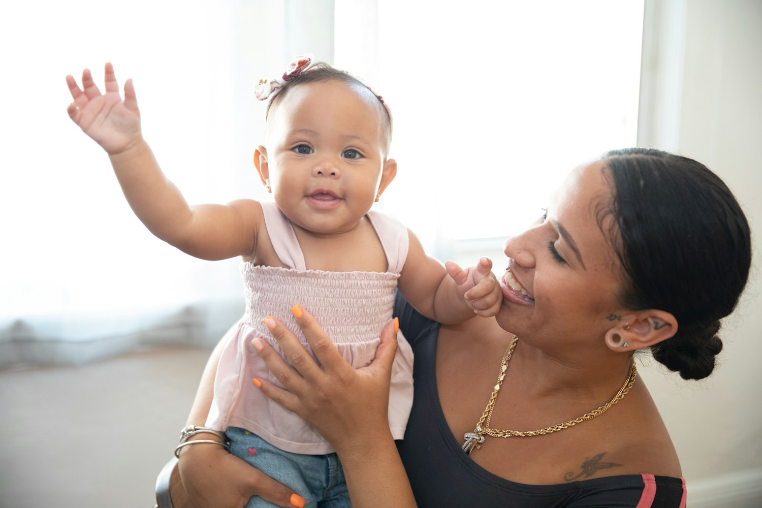 Mãe sorrindo com a filha bebê no colo, que acena para a câmera